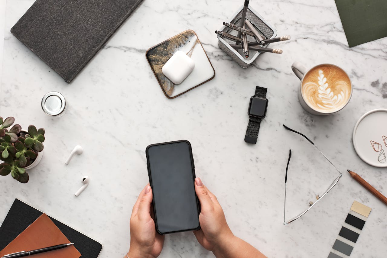 Overhead view of a stylish desk with smartphone, coffee, and office supplies on marble surface.